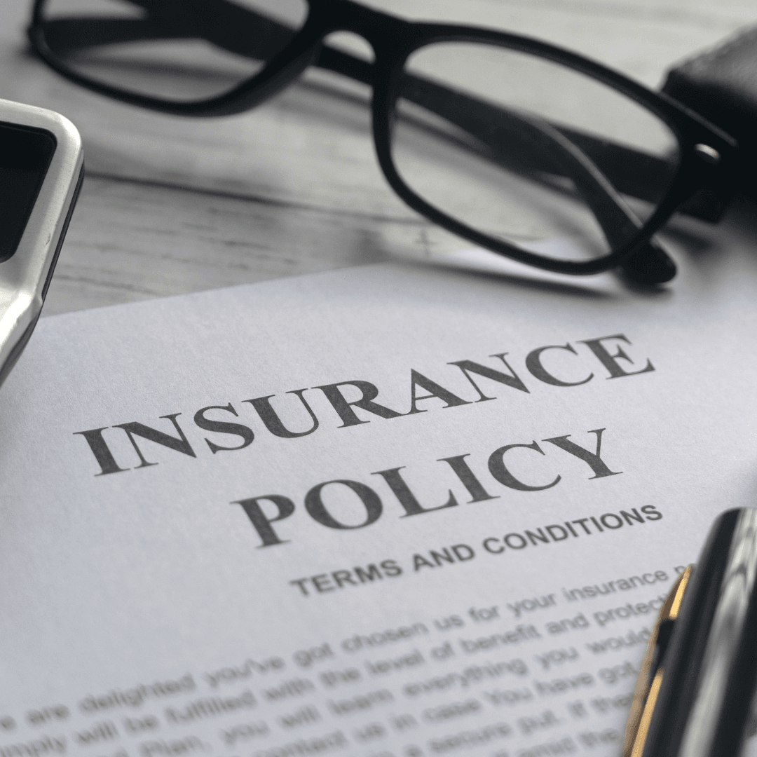 A printed insurance policy document with the title "Insurance Policy Terms and Conditions," with glasses resting on top.