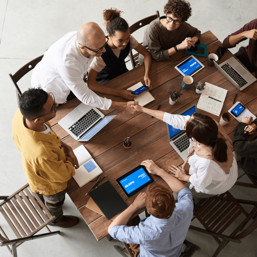  Business colleagues shaking hands over a table during a meeting with laptops and tablets.