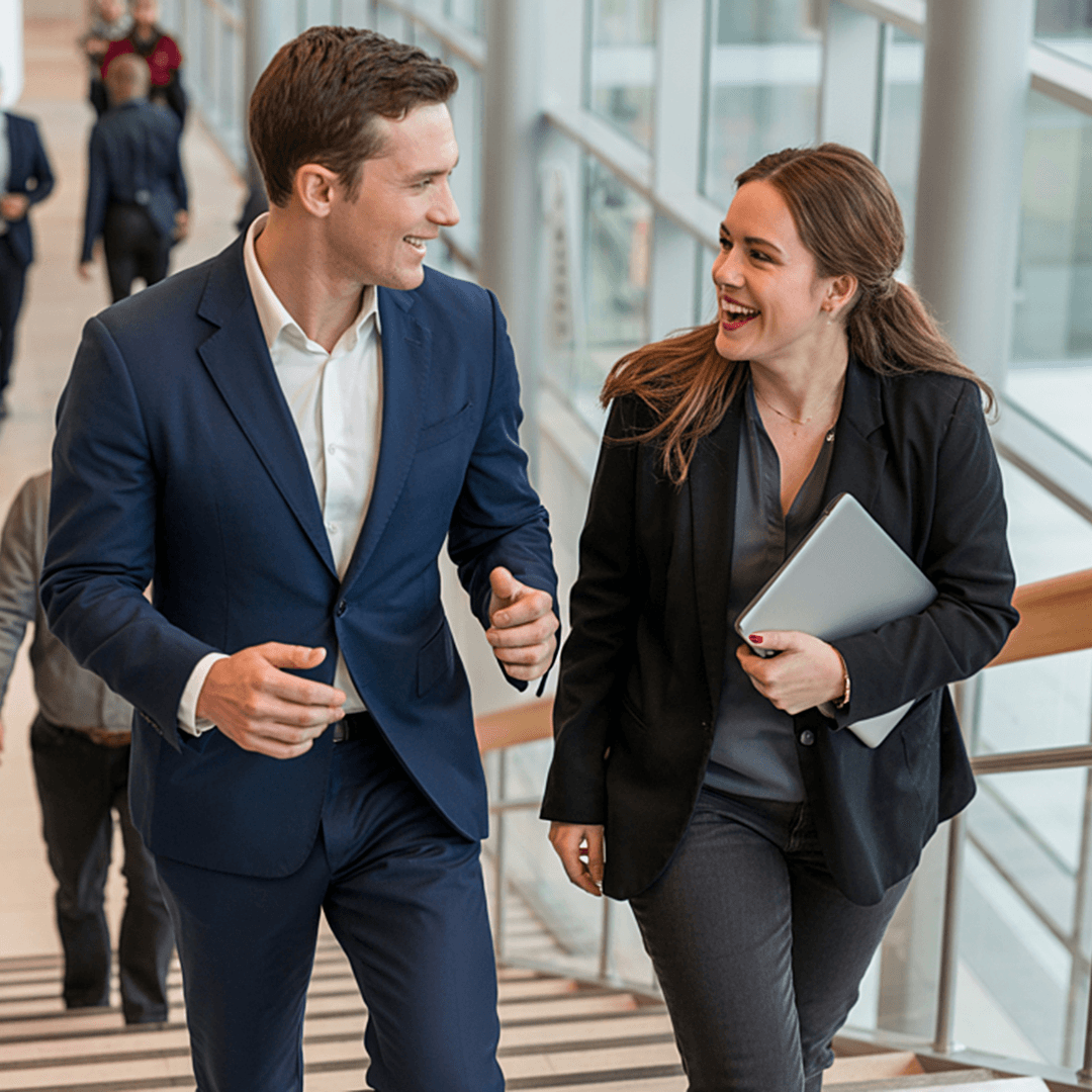 Two coworkers walking and talking together in a bright office hallway.