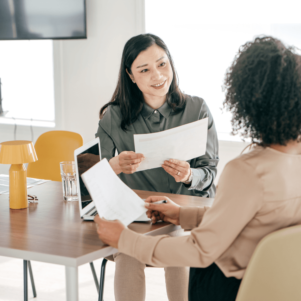 Two women review documents together at a bright office table during a benefits consultation meeting.
