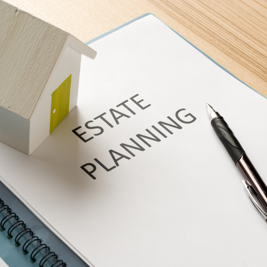 A paper document titled "Estate Planning" rests on a clipboard beside a small white model house with a yellow door and a black pen, placed on a wooden desk.