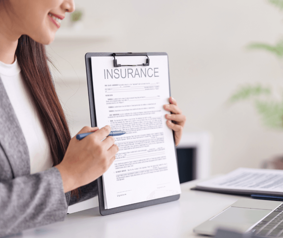 Woman reviewing insurance policy document on clipboard with laptop nearby, examining life insurance terms for potential collateral use