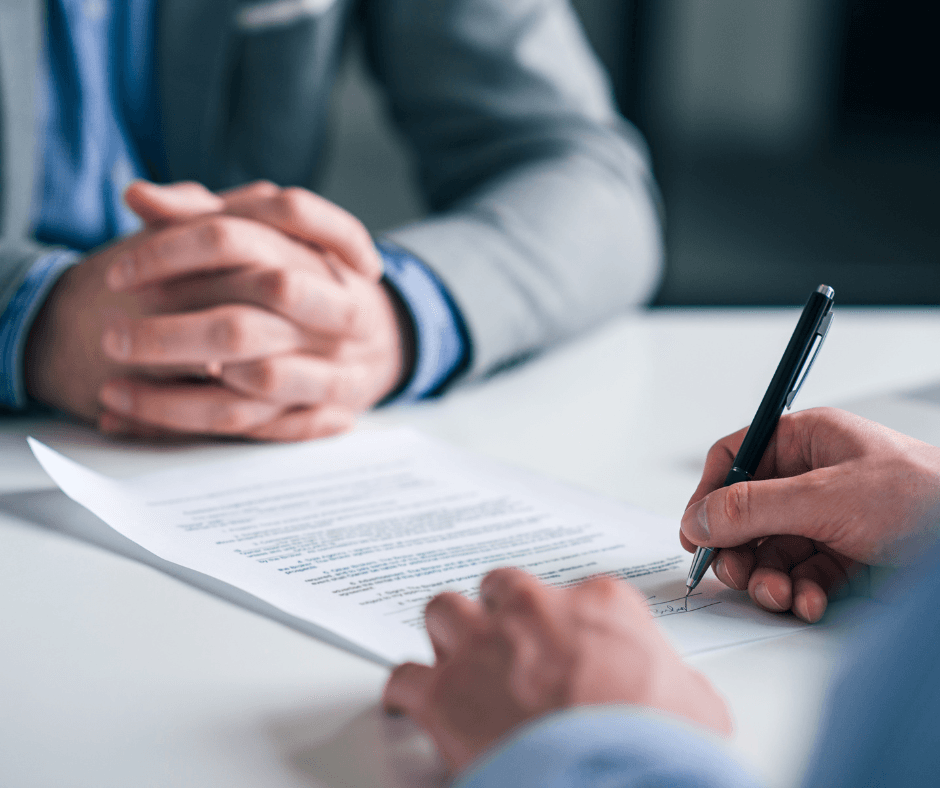 Close-up of hands signing loan documents across desk during professional meeting, finalizing collateral assignment agreement for life insurance policy
