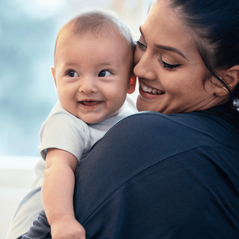 A smiling mother holds her baby close, cheek to cheek.
